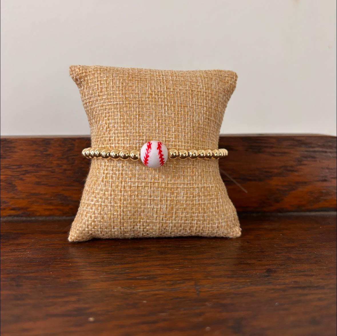 Bracelet with a baseball bead on a burlap pillow against a wooden surface