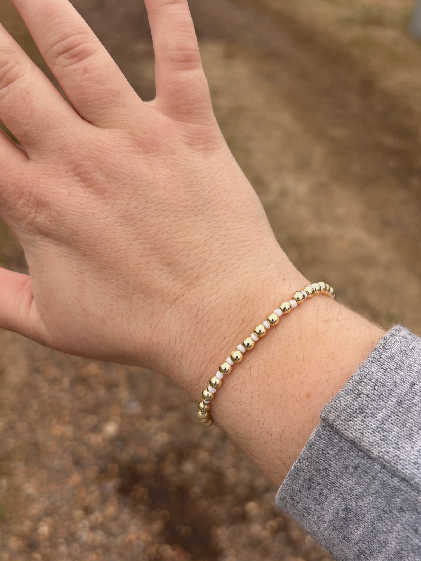 Hand wearing a gold bracelet with a blurred natural background